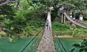 Młody mężczyzna idzie przez bambusowy most wiszący nad turkusową rzeką na Bohol, Filipiny.