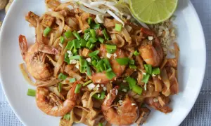 Pyszny pad thai kung z krewetkami, tofu i szczypiorkiem, podany z kiełkami fasoli mung i ćwiartką limonki.