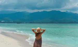 Kobieta w kapeluszu podziwia turkusowe morze i górzysty krajobraz na wyspach Gili.