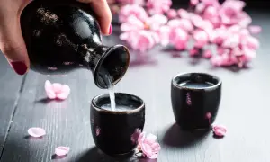 Ręka nalewa sake do czarki. Delikatne płatki wiśni i kwitnące gałązki tworzą wiosenną atmosferę, idealną do nauki, jak pić sake.