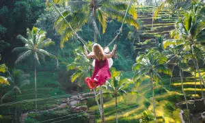 Dziewczyna na huśtawce na Bali, z wiatrem we włosach, unosi się nad tarasowymi polami ryżowymi i palmami.