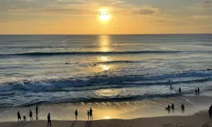 Zachód słońca na plażach Bali. Surferzy czekają na fale, a ludzie spacerują po piasku, ciesząc się złotym blaskiem.