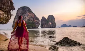 Kobieta w zwiewnej sukni spaceruje po plaży w Ao Nang, podziwiając skaliste wysepki o zachodzie słońca.