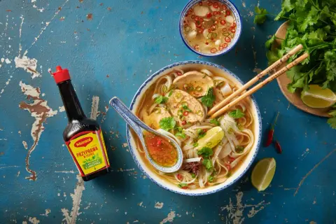 Aromatyczne pho z kurczakiem, makaronem ryżowym, limonką i kolendrą. Obok butelka Maggi, która podkreśla smak.