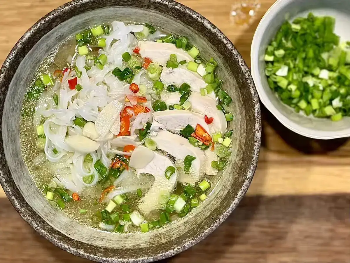 Aromatyczne zupy wietnamskie z kurczakiem, makaronem ryżowym, chili i szczypiorkiem. Obok miseczka z posiekanym szczypiorkiem.