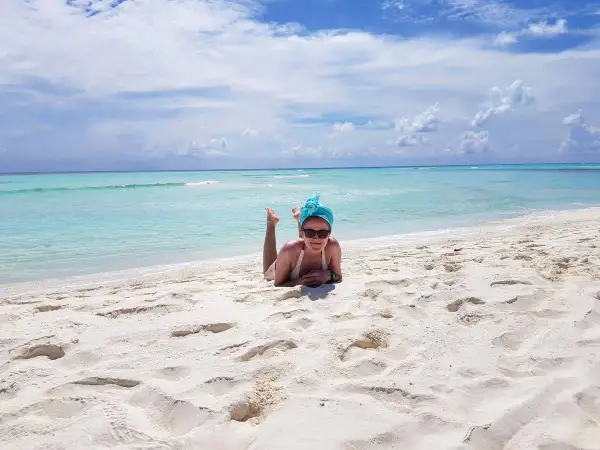 Wrzesień na Malediwach to idealna pogoda na plażowanie. Kobieta w turkusowym turbanie leży na białym piasku, ciesząc się słońcem i błękitem oceanu.